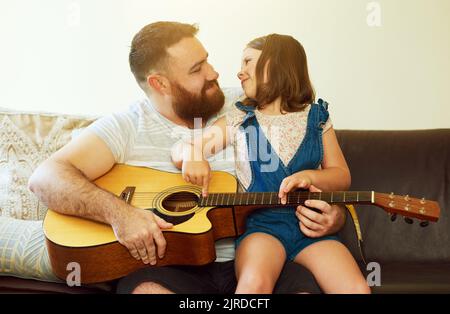 Da chi meglio imparare del padrone stesso. Una ragazza adorabile che suona la chitarra con il padre a casa. Foto Stock