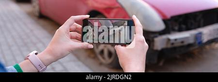 Le mani femminili scattano le foto dei danni dell'automobile sul primo piano del telefono mobile Foto Stock