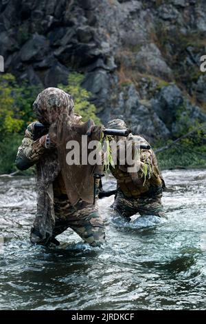 Foto verticale di due soldati militari mercenari durante una missione di sabotaggio dietro le linee nemiche - si trova in piedi ginocchio nel fiume e mira alla it Foto Stock