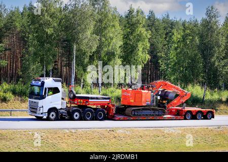 Il camion bianco Volvo FH16 di Eilola Logistics Oy tira l'escavatore Hitachi Zaxis 225 su un rimorchio caricatore basso Faymonville su strada. Salo, Finlandia. Luglio 17, 20. Foto Stock