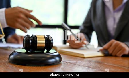 Un gavel del giudice o un martello del giudice è sulla scrivania dell'ufficio di legno sopra lo sfondo sfocato un avvocato che si riunisce con il suo cliente. Immagine di primo piano Foto Stock