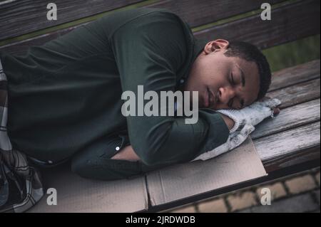 Uomo dalla pelle scura che dorme su cartone sulla panca Foto Stock