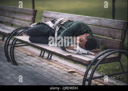 Uomo dalla pelle scura sdraiato sulla panca del parco Foto Stock