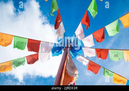Colorate bandiere di preghiera buddiste tibetane appese su un palo, che sventolano sotto il cielo blu vicino al tempio buddista di Tagong. Foto Stock