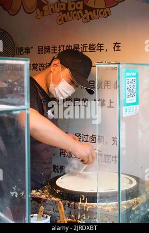 Un uomo che indossa una maschera contro l'inquinamento che fa pancake cinese chiamato Jianbing, un cibo di strada cinese tradizionale. Foto Stock