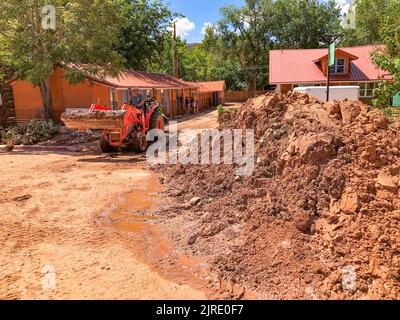 Un volontario su un piccolo trattore raschia il fango da un parcheggio e lo accumula per strada il giorno dopo un'alluvione lampo a Moab, Utah. Foto Stock