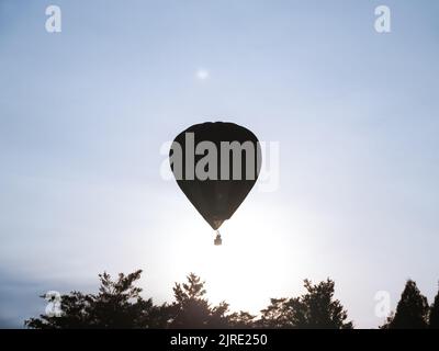 Nella silhouette, la mongolfiera si sposta attraverso l'atmosfera sopra le cime degli alberi e attraverso il cielo blu. Foto Stock