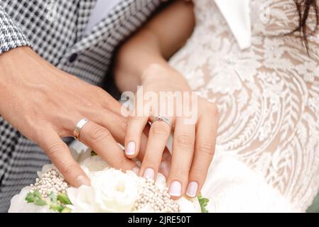 Sposi novelli che tengono le mani, che tengono le mani in primo piano, primo piano delle mani di giovane coppia con anelli di nozze sulle barrette dell'anello Foto Stock