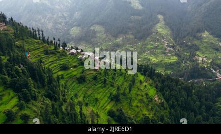 Cima aerea giù delle montagne di Jibhi sul pomeriggio nuvoloso e case che si affacciano sulla valle Foto Stock