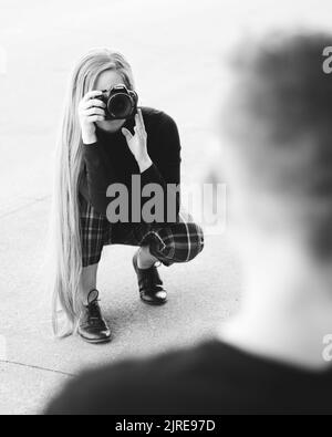 Ripresa verticale in scala di grigi di una donna con capelli lunghi che scatta foto con una fotocamera professionale Foto Stock