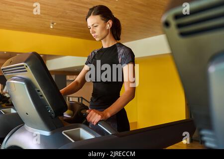 Giovane donna in abbigliamento sportivo a piedi sul tapis roulant mentre si allenano nel centro benessere Foto Stock
