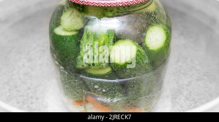 Un vasetto di cetrioli viene cotto in una pentola di acqua bollente. Foto Stock