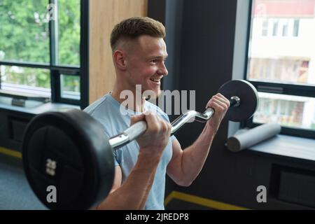 Giovane uomo sorridente che solleva il barbell durante l'allenamento sportivo in palestra Foto Stock