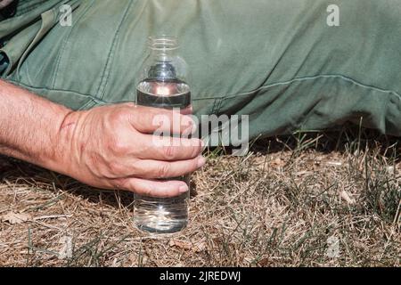 Il contadino siede sul suo prato e tiene in mano una bottiglia d'acqua. Foto Stock