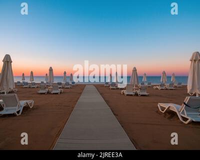 Ombrelloni e lettini sulla tranquilla spiaggia di mare all'alba Foto Stock