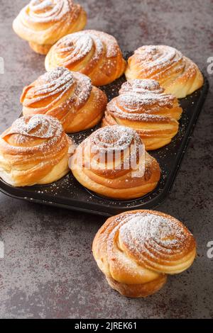 Crocini sfridati e burrosi e ricoperti di zucchero a velo nella teglia per muffin sul tavolo. Verticale Foto Stock