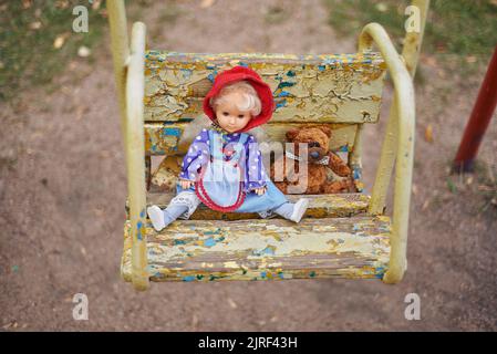 bambola giocattolo e orsacchiotto su un'altalena per bambini nel parco giochi Foto Stock