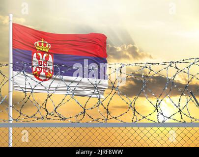 Flagpole con la bandiera della Serbia contro il cielo e dietro una recinzione con filo spinato. Il concetto di protezione delle frontiere dei territori. Foto Stock