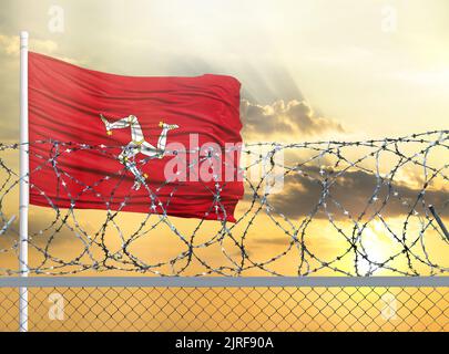 Flagpole con la bandiera dell'Isola di Man contro il cielo e dietro una recinzione con filo spinato. Il concetto di protezione delle frontiere dei territori. Foto Stock
