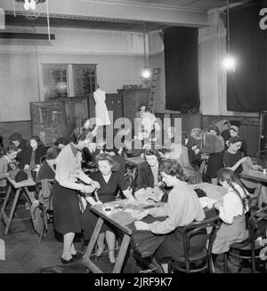 Il MEND e far fare- sartoria in classi di Londra, 1943 Donne sedere ai tavoli e lavorare con ago e filo durante una sartoria classe in una scuola a Brixton. In piedi in primo piano per aiutare una delle donne è Miss Clifford, un London County Council instructress. La LCC è stato in esecuzione per tali classi per molti anni, ma la loro popolarità è cresciuta a partire dallo scoppio della guerra e dell'introduzione di vestiti razionamento e far fare e Mend. Secondo la didascalia originale, Miss Clifford giacca è stata realizzata di una coppia di bianco pantaloni di flanella. Una delle figlie delle donne può als Foto Stock