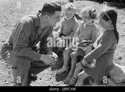 Le truppe USA in un Villaggio Inglese- La vita di tutti i giorni con gli americani in Burton Bradstock, Dorset, Regno Unito 1944 Sergente Foster Whitsitt (di Route 4, CASELLA 915, Vancouver, Washington) sorrisi a tre bambini locali a cui ha appena dato le arance, sotto il sole nel villaggio di Burton Bradstock, Dorset. I bambini includono Chris Kerley e Betty 'lentiggini' Mackay (a destra). Betty è stato dato il soprannome di "lentiggini' dagli americani, come era un "camp favorito". Foto Stock