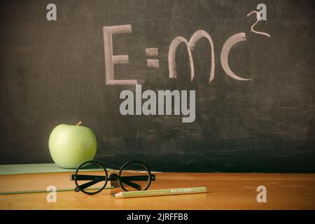 Equazione e=mc2 scritta a mano su lavagna con mela e libro Foto Stock