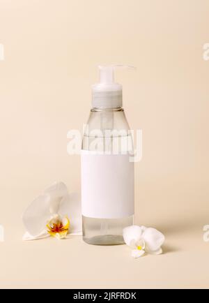 Dispenser per dispenser per cosmetici vicino a fiori di orchidee bianche su primo piano beige chiaro, mockup. Pacchetto prodotti di bellezza per la cura della pelle. Cosmetici naturali esotici, p Foto Stock