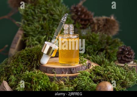 Flacone contagocce aperto con liquido giallo vicino al muschio verde, primo piano. Prodotti di bellezza per la cura della pelle, siero o olio essenziale, concetto cosmetico biologico naturale Foto Stock