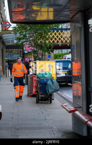 LONDRA - 20 maggio 2022: Pulitore stradale in abbigliamento arancione riflettente con carretto antipolvere al di fuori della stazione di Waterloo Foto Stock