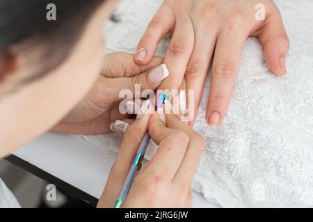 dettaglio delle mani di una ragazza manicurista latina, tenendo il dito della donna per eseguire la corretta pulizia della cuticola con lo spintore della cuticola Foto Stock