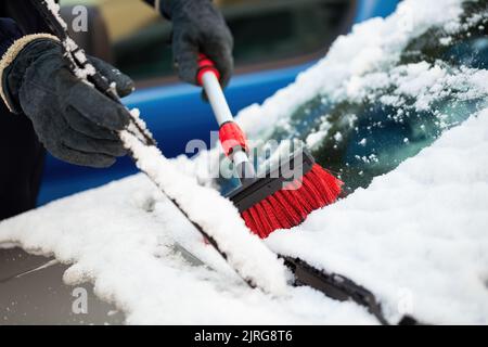 Uomo in guanti che solleva il tergicristallo e spazzolano via la neve Foto Stock