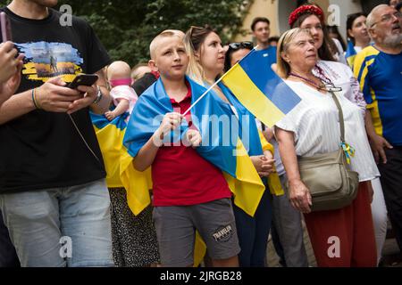 I rifugiati ucraini sventolano bandiere durante l'evento nazionale di canto dell'inno a Varsavia. Decine di rifugiati ucraini si sono riuniti all'esterno della "Casa Ucraina" (Dom Ukrainski) a Varsavia per cantare l'inno nazionale dell'Ucraina come parte di un progetto di canto globale dell'inno. È quello di unire gli ucraini in tutto il mondo e di stabilire un record per la performance globale simultanea dell'inno. Anche gli ucraini volevano celebrare la giornata dell'indipendenza dell'Ucraina e protestare contro l'invasione russa di sei mesi iniziata il 24th febbraio. Foto Stock