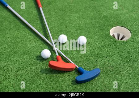 Putters e palle da golf in miniatura assortiti si inclinano su erba sintetica. Foto Stock