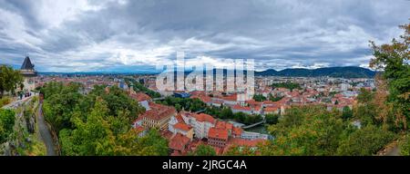 Paesaggio urbano della città vecchia di Graz e la Torre dell'Orologio (Grazer Uhrturm), famosa attrazione turistica a Graz, Steiermark, Austria, in nuvoloso giorno d'estate. Foto Stock