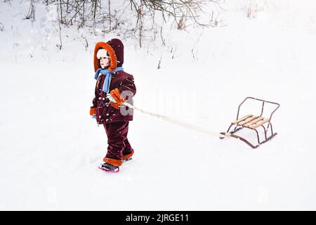 Bambino che tira una slitta nella neve. Il bambino sta cavalcando su una slitta. I bambini giocano all'aperto sulla neve, i bambini si divertirono. Foto Stock