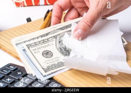 Mano di una donna che tiene un assegno vuoto e denaro dollari, contando denaro su una calcolatrice, primo piano. Il concetto di spese di pianificazione, tasse. Piano di bilancio Foto Stock