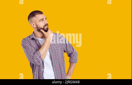 Uomo isolato su sfondo giallo, guardando lo spazio copia e pensando a qualcosa Foto Stock