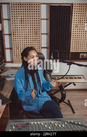 Affascinante donna africana presentatore radio parla in microfono mentre trasmette interessante programma in studio di registrazione Foto Stock