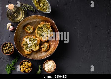 Bistecca di cavolfiore con spezie, salsa di chimichurri, fiocchi di mandorle. Capperi, olive, erbe, fianco a fianco. Sfondo scuro. Cibo vegetariano. CopySpace. Foto Stock