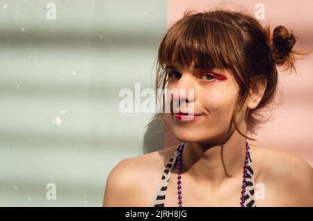 ritratto di giovane donna transgender latina ridendo e guardando la fotocamera all'aperto su uno sfondo rosa e verde parete Foto Stock