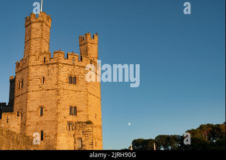 Caernarfon, Regno Unito - 10 luglio 2022: Caldo bagliore della luce del suset sulla Eagle Tower del Castello di Caernarfon nel Galles del Nord Foto Stock