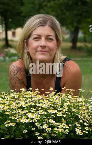 Ritratto di una donna bionda dietro bellissimi fiori margherite nei colori giallo e verde Foto Stock