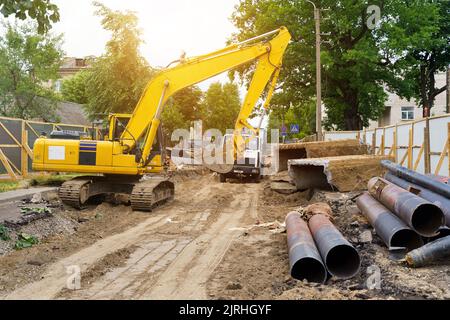 Un escavatore in un cantiere, vicino a tubi metallici, materiali da costruzione e macchinari. Concetto di costruzione Foto Stock