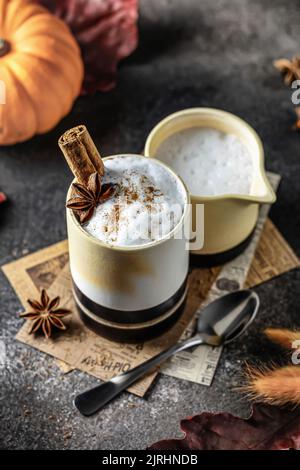 Latte piccante di zucca o cacao in vetro ceramico con crema e cannella. Accogliente bevanda calda autunno concetto con zucche Foto Stock