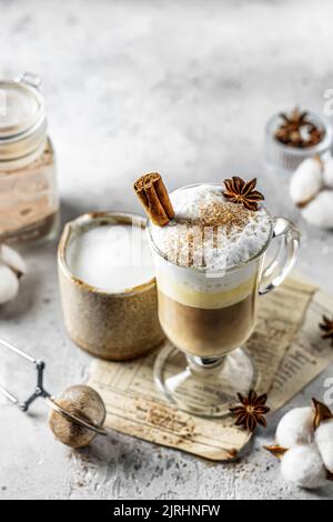 Latte piccante di zucca in vetro con panna e cannella. Accogliente bevanda autunnale calda su sfondo grigio chiaro con spazio testo Foto Stock