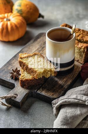 Due fette di pane di zucca su asse di legno con un bicchiere di tè e zucche sullo sfondo. Dessert autunnale Foto Stock