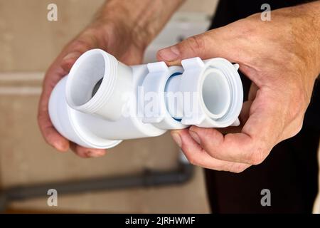 L'idraulico ispeziona le perdite di sifone di plastica dallo scarico del lavandino nel bagno. Foto Stock