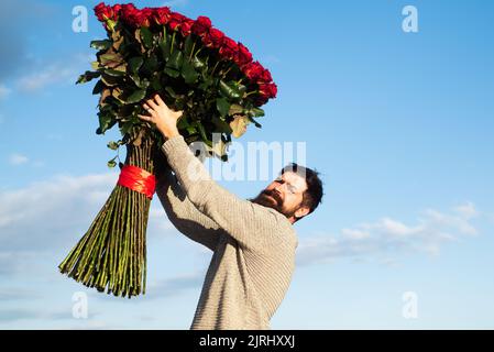 Uomo con fiori rose. Happy man tiene un grande bouquet di rose rosse, proporre al fidanzato in data. Romantico ragazzo celebrare San Valentino. Foto Stock