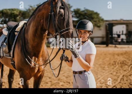 ritratto di giovane donna in abbigliamento da equitazione in posa con cavallo prima di dressage con casco Foto Stock