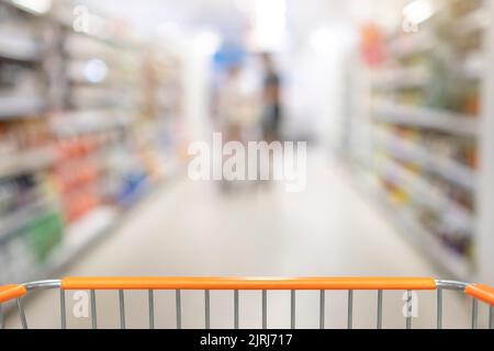 Corridoio sfocato del supermercato con scaffali di merce e un carrello in primo piano Foto Stock